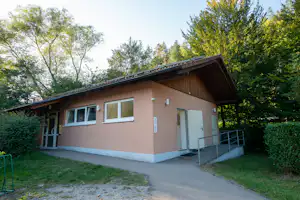 Campinghaus mit Eingangstür, Fenstern und Treppe am Weg, umgeben von Bäumen im Grünen.