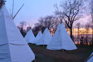 Tipi-Zelte auf einem Campingplatz im Wald, mit Blick auf Bäume und den Sonnenuntergang am Himmel.