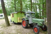 Schwielowsee-Camping - Zirkus Wohnwagen mit Traktor davor zwischen Bäumen