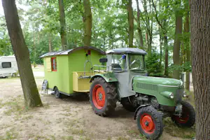Schwielowsee-Camping - Zirkus Wohnwagen mit Traktor davor zwischen Bäumen
