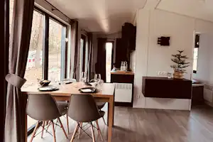 Essbereich in einem Mobilhome: Holztisch mit Stühlen, große Fensterfront und Blick auf die Terrasse.