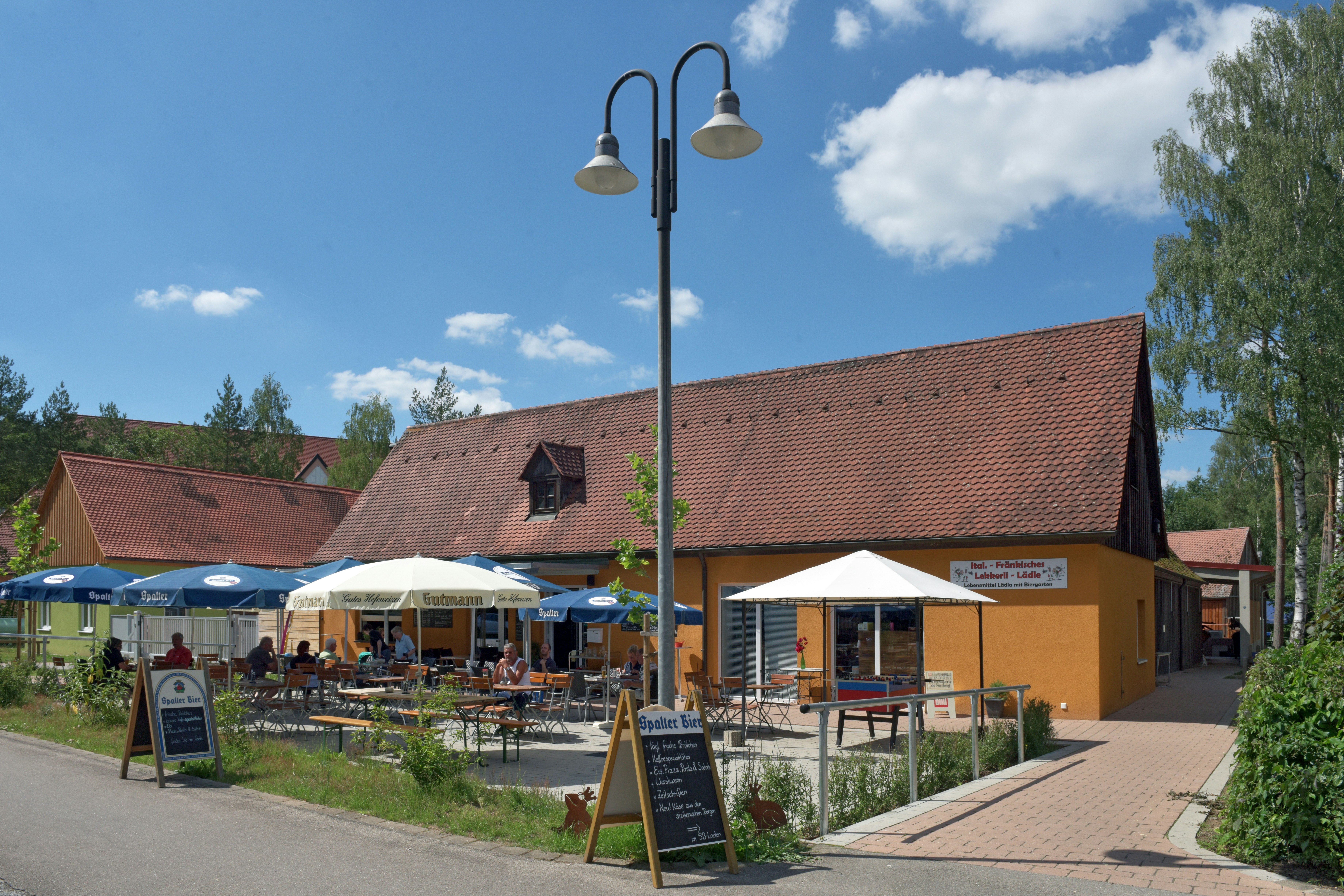 Seecamping Langlau - Biergarten mit Sonnenschirmen und Supermarkt auf dem Campingplatz