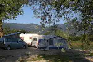 Wohnmobil und Transporter neben einem Zelt am See, im Hintergrund bewaldete Hügel und Bäume.