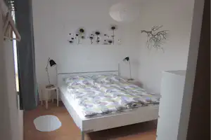 Bett mit gemusterten Decken, zwei Stehlampen und Nachttischen in einem hellen Schlafzimmer mit Blumenbild an der Wand.