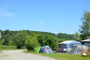 Campingzelte auf dem Stellplatz, im Hintergrund dichtes Grün und ein großer blauer Himmel.