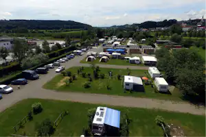 Luftaufnahme eines Campingplatzes mit Wohnmobilen, Zelten und Stellplätzen, umgeben von Wiesen, Bäumen und einem Weg.