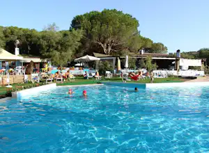 Großer Camping-Pool mit Liegen und Sonnenschirmen, im Hintergrund Bäume und ein weißes Gebäude.