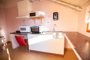 Küchenzeile im Campingunterkunftsraum mit Spüle, Herd, Mikrowelle und Schränken, daneben Fenster und Wandregal.