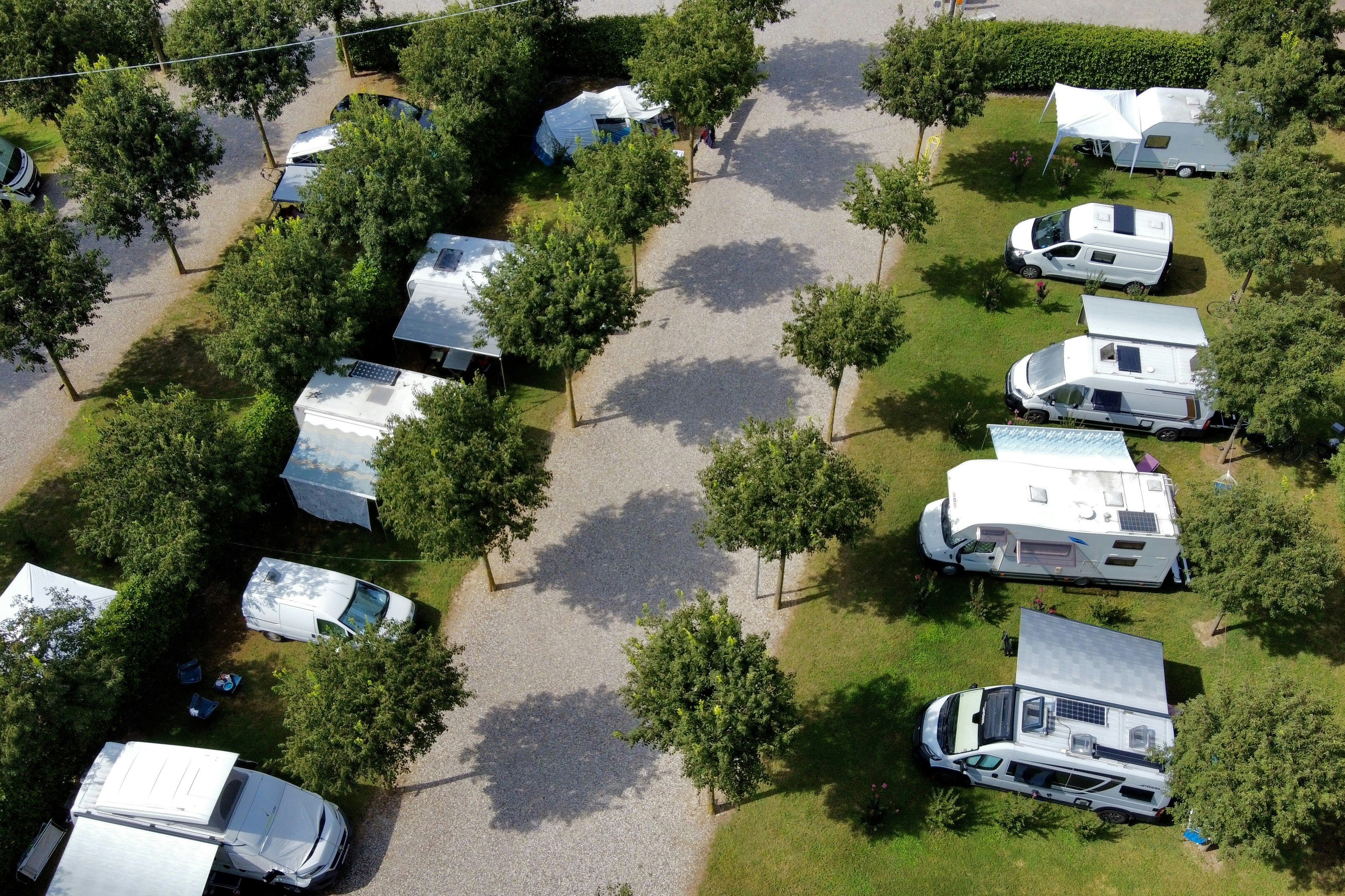 Wohnmobile auf Stellplätzen im Grünen, zwischen Bäumen und Wegen auf einem Campingplatzgelände.