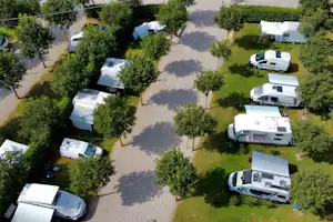 Wohnmobile auf Stellplätzen im Grünen, zwischen Bäumen und Wegen auf einem Campingplatzgelände.
