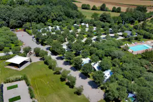 Luftaufnahme eines Campingplatzes im Grünen mit Stellplätzen, Wegen, einem weißen Zelt und einem Pool.