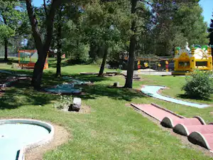 Campingplatz mit Rasenfläche, Spielplatz mit gelben Rutschen und Trampolin, daneben runde Planschbecken und Wege.