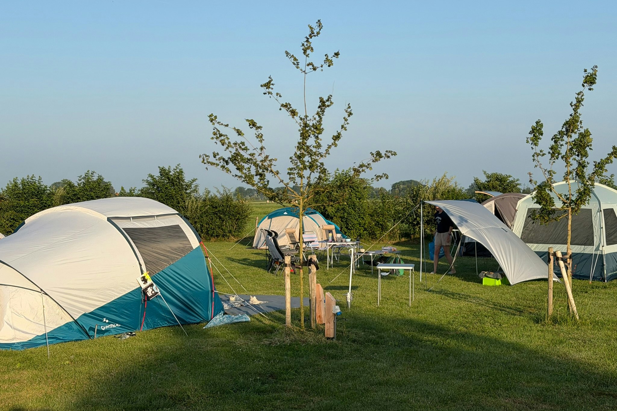 Zelte auf einem Campingplatz mit Rasenfläche, Holzpfosten und Sitzgelegenheiten zwischen den Zelten.