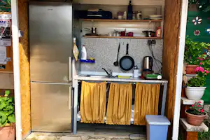 Küchenzeile im Campingbereich mit Kühlschrank, Herd, Pfanne, Wasserkocher und Gewürzregal auf Granitplatte.