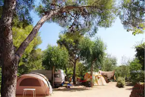 Zelte und ein Wohnwagen auf einem Campingplatz zwischen Bäumen, mit Tisch und Stühlen am Stellplatz.