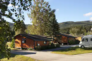Holzhütten am Campingplatz mit gepflastertem Weg, Rasenfläche und geparktes Wohnmobil vor den Gebäuden.
