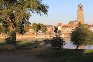 Blick auf den Fluss mit Bäumen im Vordergrund und einen Kirchturm über den Häusern am Ufer.