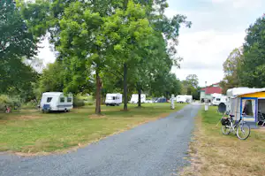 Wohnmobile und Zelt auf einem Campingplatz, gepflasterter Weg, Rasenfläche und Bäume im Hintergrund.