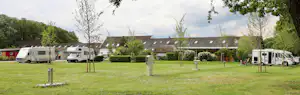 Stellplätze auf einem Campingplatz mit Wohnmobilen und Wohnwagen, Rasenfläche, Hecken und Bäumen im Hintergrund.