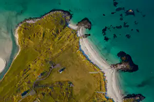 Luftaufnahme einer kleinen Insel mit türkisfarbenem Wasser, Sandstrand und schmalen Wegen entlang der Küste.