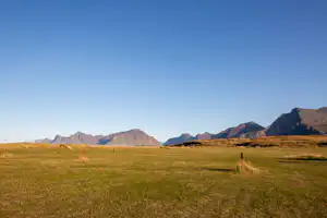 Weite grüne Wiese mit Pfad, im Hintergrund hohe Berge und klare Sicht in einer alpinen Landschaft.