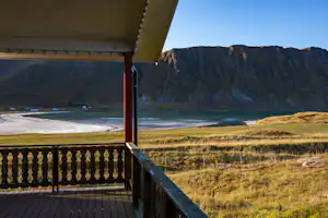 Balkon eines Campingplatzes mit Holzgeländer, Blick auf Wiese, Küste und Berge in der Ferne.