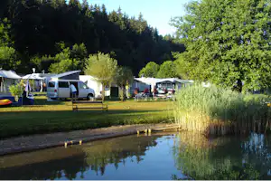 Campingplatz mit Wohnmobilen und Zelten am Seeufer, Rasen und Bäume im Hintergrund.