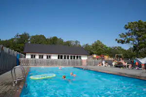 Schwimmbecken auf dem Campingplatz mit Liegen am Rand und einem Gebäude im Hintergrund.