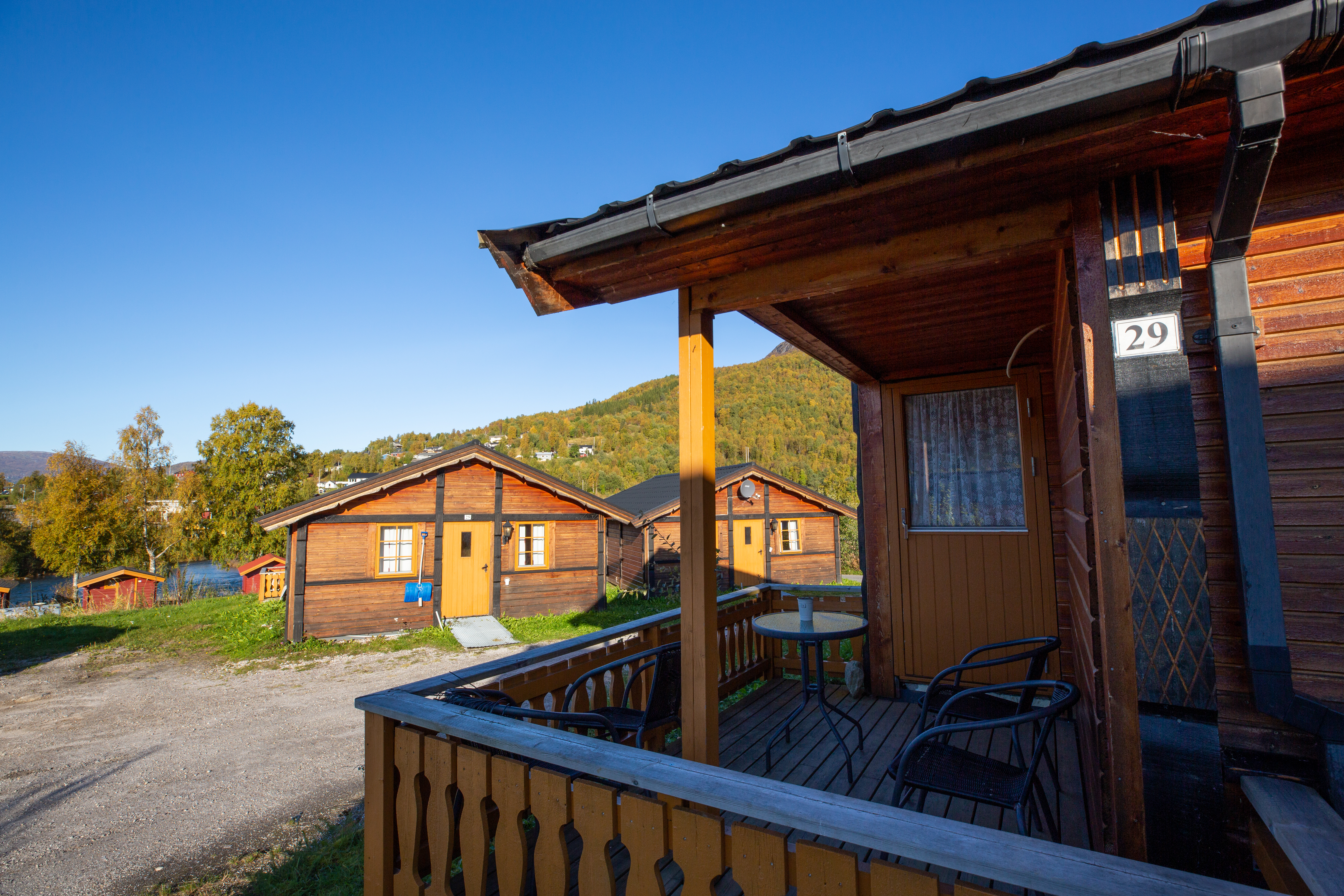 Holzhaus mit Terrasse und Sitzgruppe, Nummer 29 am Eingang, daneben weitere Ferienhäuser und ein Weg auf dem Campingplatz.