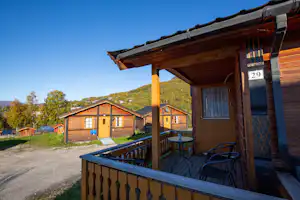 Holzhaus mit Terrasse und Sitzgruppe, Nummer 29 am Eingang, daneben weitere Ferienhäuser und ein Weg auf dem Campingplatz.