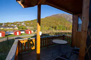 Balkon mit Tisch und Stühlen, Blick auf Campingplatz mit roten Hütten und Berge im Hintergrund.