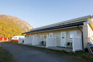 Mobilheim am Campingplatz mit Terrasse, weißen Sichtschutzwänden, zwei Stühlen und Blick auf die Berge im Hintergrund.