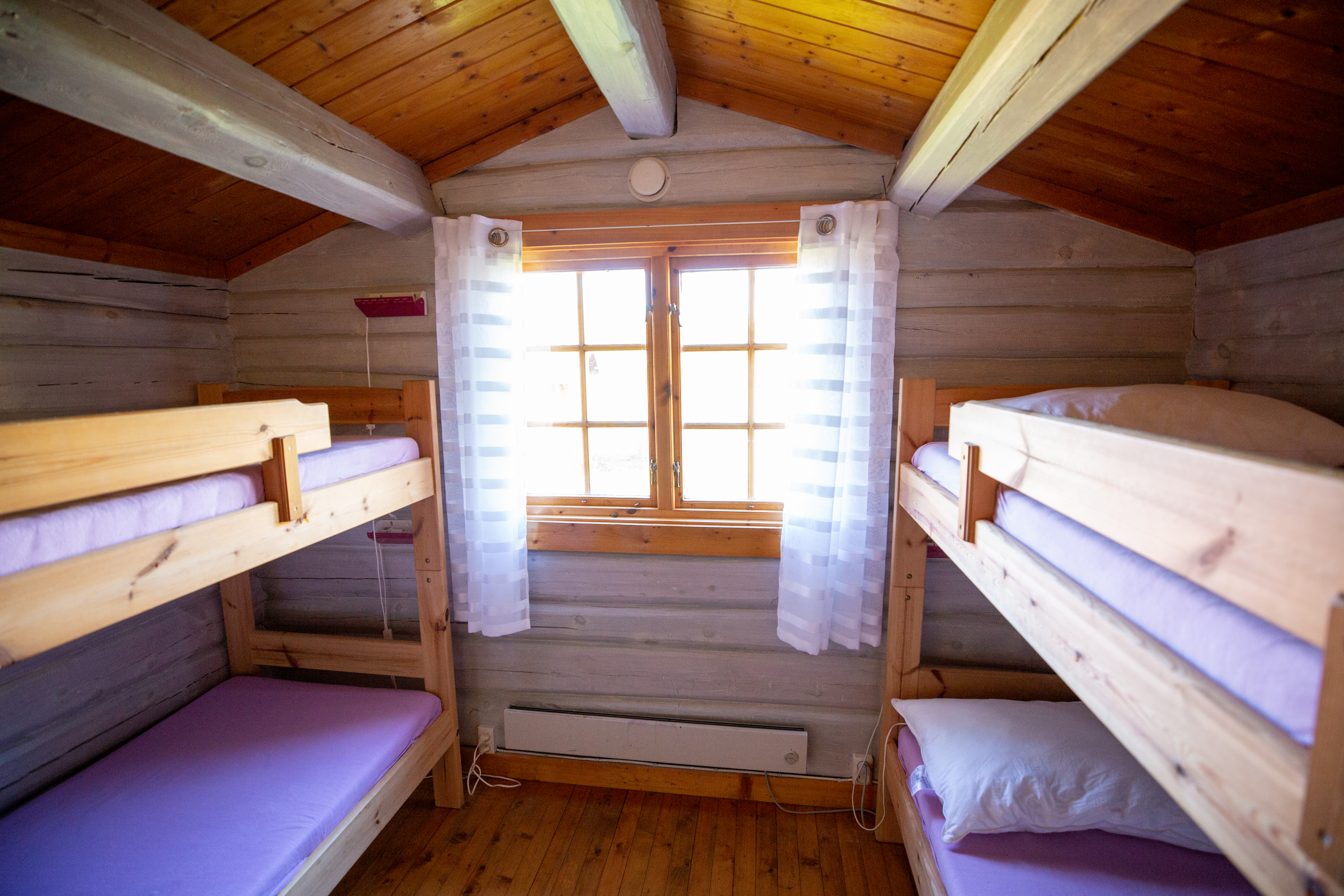 Holz-Campingzimmer mit zwei Etagenbetten, Fenster mit Vorhängen und Holzboden, Blick auf die Betten und den Raum.