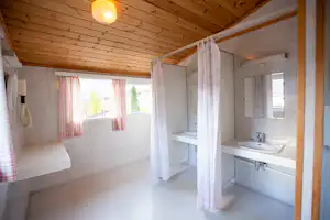 Badezimmer in einem Wohnwagen mit Waschbecken, Dusche und Vorhang, Holzdecke und Fenster mit Vorhängen.