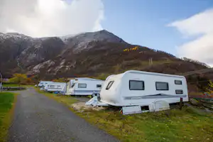 Wohnwagen auf einem Campingplatz am Weg, im Hintergrund Berge und ein Tal mit Wohnmobilen.