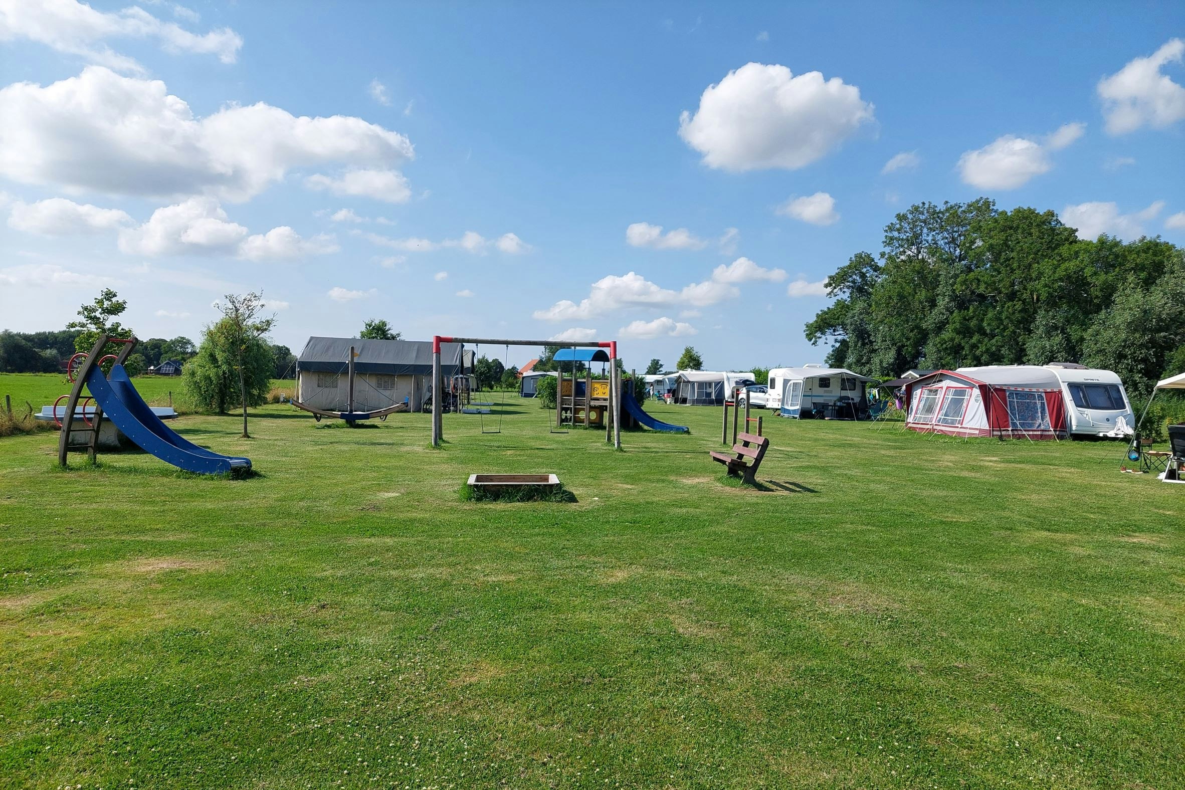 Swichumer Pleats - Blick auf die Wiese mit Standplätzen und den Spielplatz mit kleinem Sandkasten, Schaukeln und Rutschen