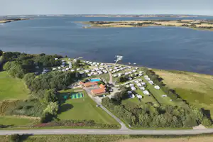 Luftaufnahme eines Campingplatzes am See mit Stellplätzen, Wegen, Gebäuden und Grünflächen in hügeliger Landschaft.