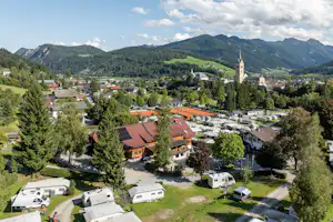 Campingplatz mit Wohnwagen und Stellplätzen, Blick auf ein Dorf mit Kirche und Berge im Hintergrund.