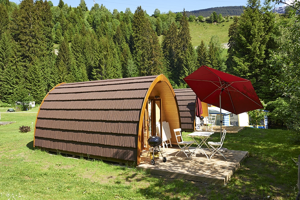 TCS-Camping Disentis - Mobilheim mit kleiner Terrasse Grill und Sonnenschirm auf dem Campingplatz