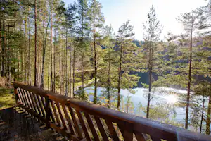 Holzterrasse mit Geländer über dem Wald, Blick auf einen See mit Sonnenreflexen zwischen den Bäumen.