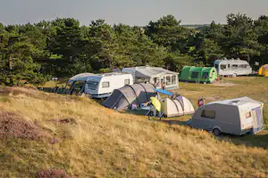 Campingplatz mit mehreren Wohnwagen und Zelten auf einem Hang, im Hintergrund Bäume und ein Wohnmobil.