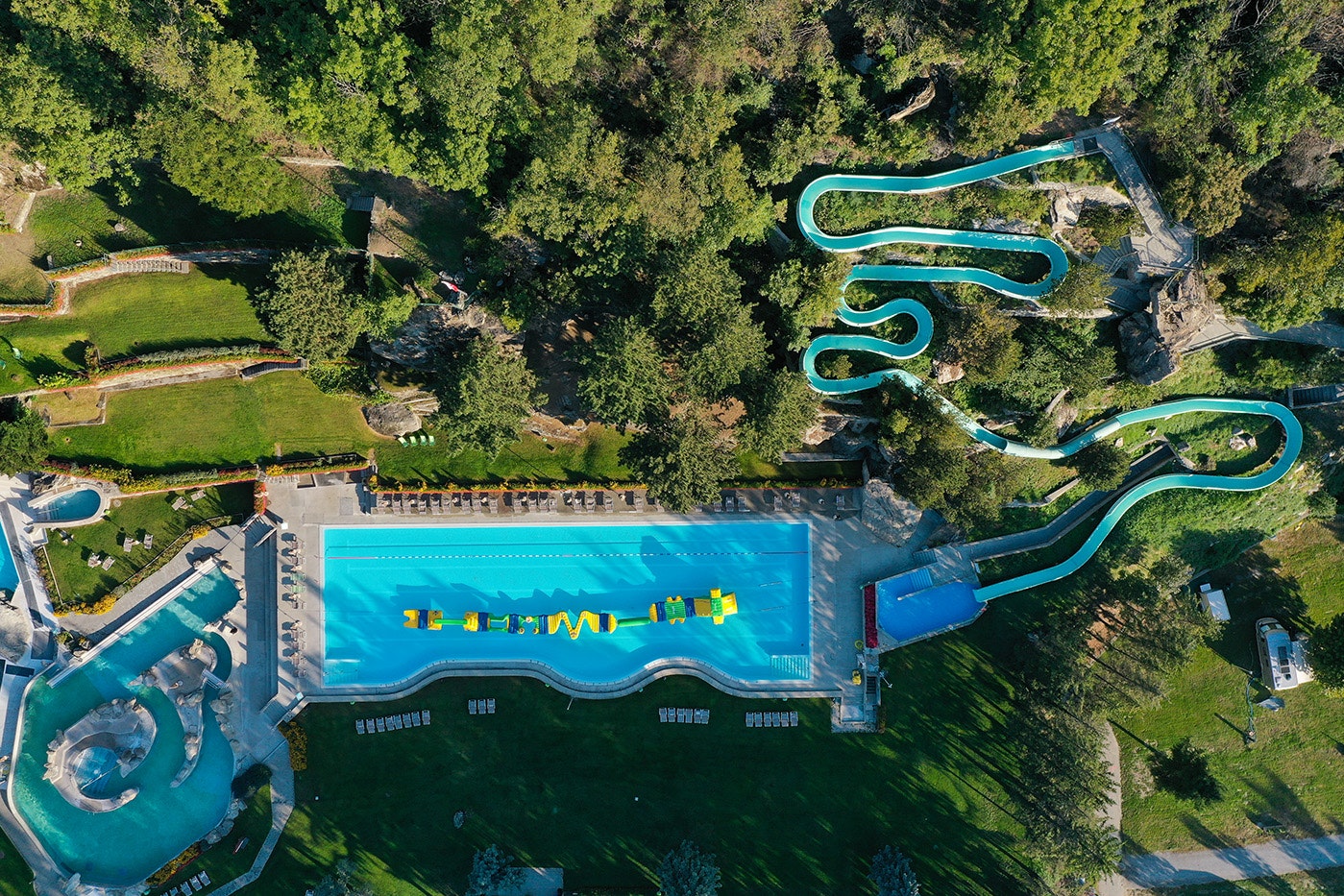 Luftaufnahme eines Campingplatzes mit großem Pool, mehreren Rutschen und Becken, umgeben von Grünflächen und Wegen.