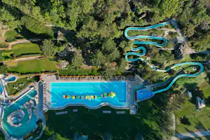 Luftaufnahme eines Campingplatzes mit großem Pool, mehreren Rutschen und Becken, umgeben von Grünflächen und Wegen.