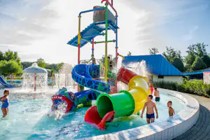 Bunte Wasserrutschen im Camping-Pool mit Spritzwasser, Kinder im Becken und Rutsche mit Treppe und Plattform.