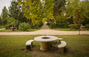 Thermalcamping Castrum Hajdúböszörmény - Brunnen mit Bänken auf der Wiese im Schatten der Bäume auf dem Campingplatz