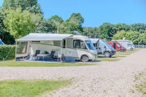 Wohnmobil auf dem Campingplatz mit Vorzelt, Tisch und Stühlen, daneben weitere Fahrzeuge und Bäume im Hintergrund.