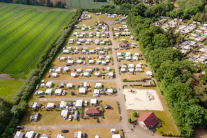 Luftaufnahme eines Campingplatzes mit vielen Wohnmobilen und Wohnwagen, Wegen, Bäumen und einem kleinen Sportplatz.