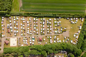 Luftaufnahme eines Campingplatzes mit vielen Stellplätzen, kleinen Wohnwagen und Zelten, Wegen und Grünflächen zwischen den Parzellen.