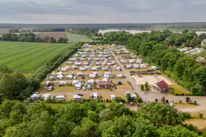 Luftaufnahme eines Campingplatzes mit vielen Stellplätzen, Wohnwagen und Zelten, umgeben von Bäumen und Feldern.