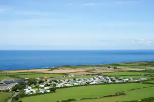 Campingplatz in Küstennähe, Luftaufnahme mit Wohnwagen und Zelten, grünen Wiesen und Blick auf das Meer.